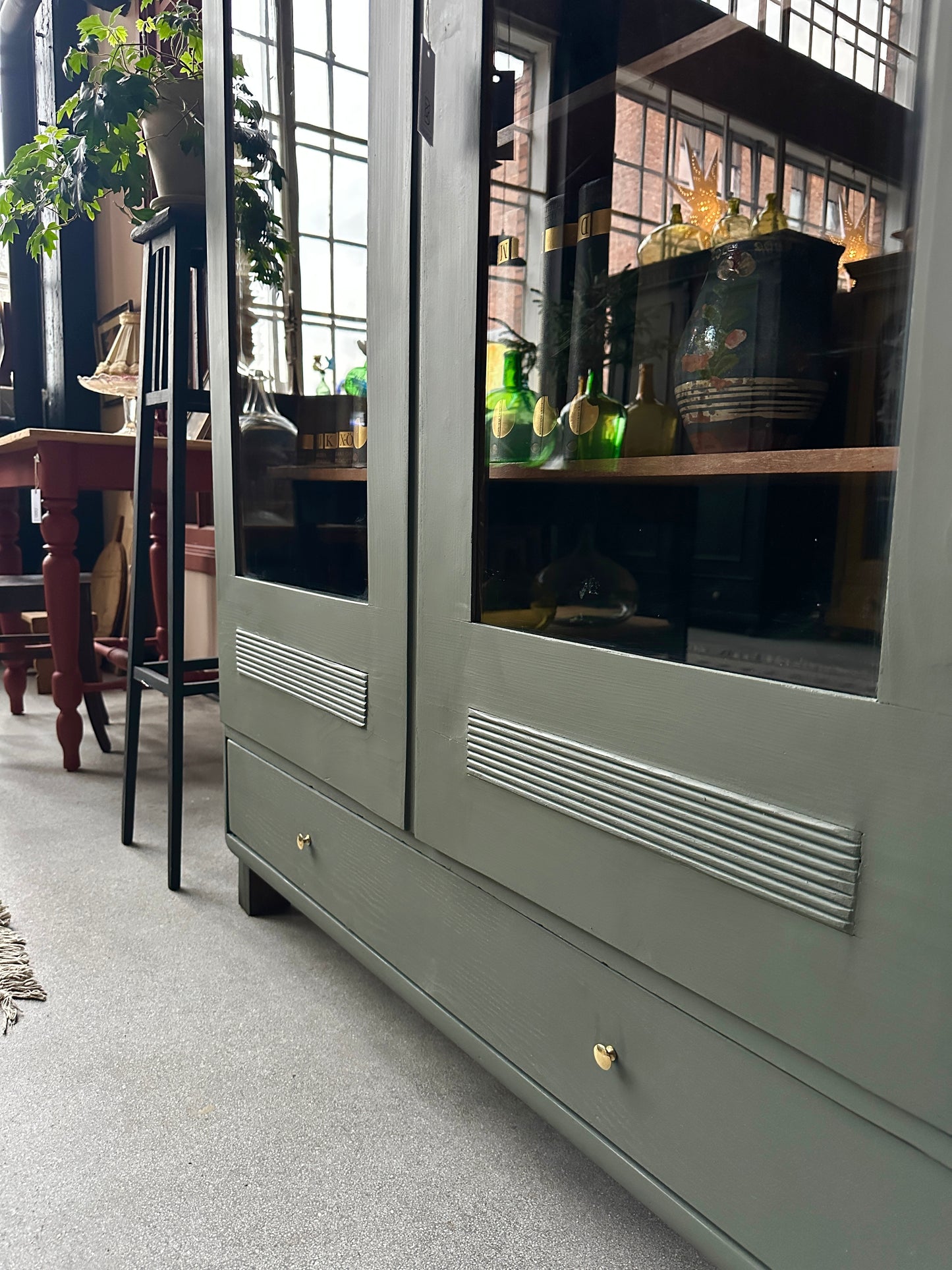 Ett gammalt vackert vitrinskåp men raka och mjuka former och enkla detaljer. Skåpet har en bred praktiskt låda nertill med nya knoppar i äldre stil.