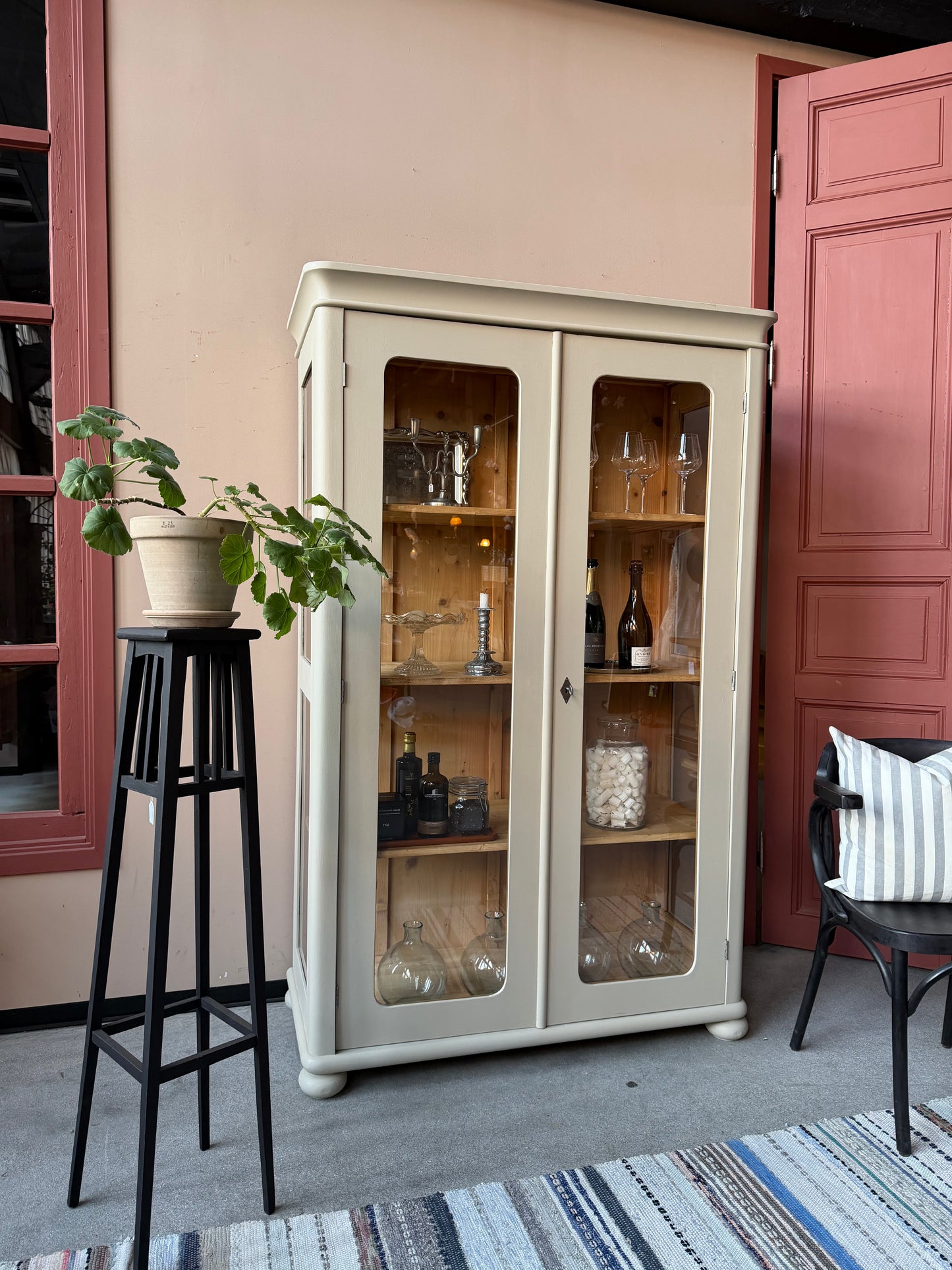 Ett vackert gammalt vitrinskåp i Greige med runda former och hela glaspartier i dörrarna och vitrin i sidorna.