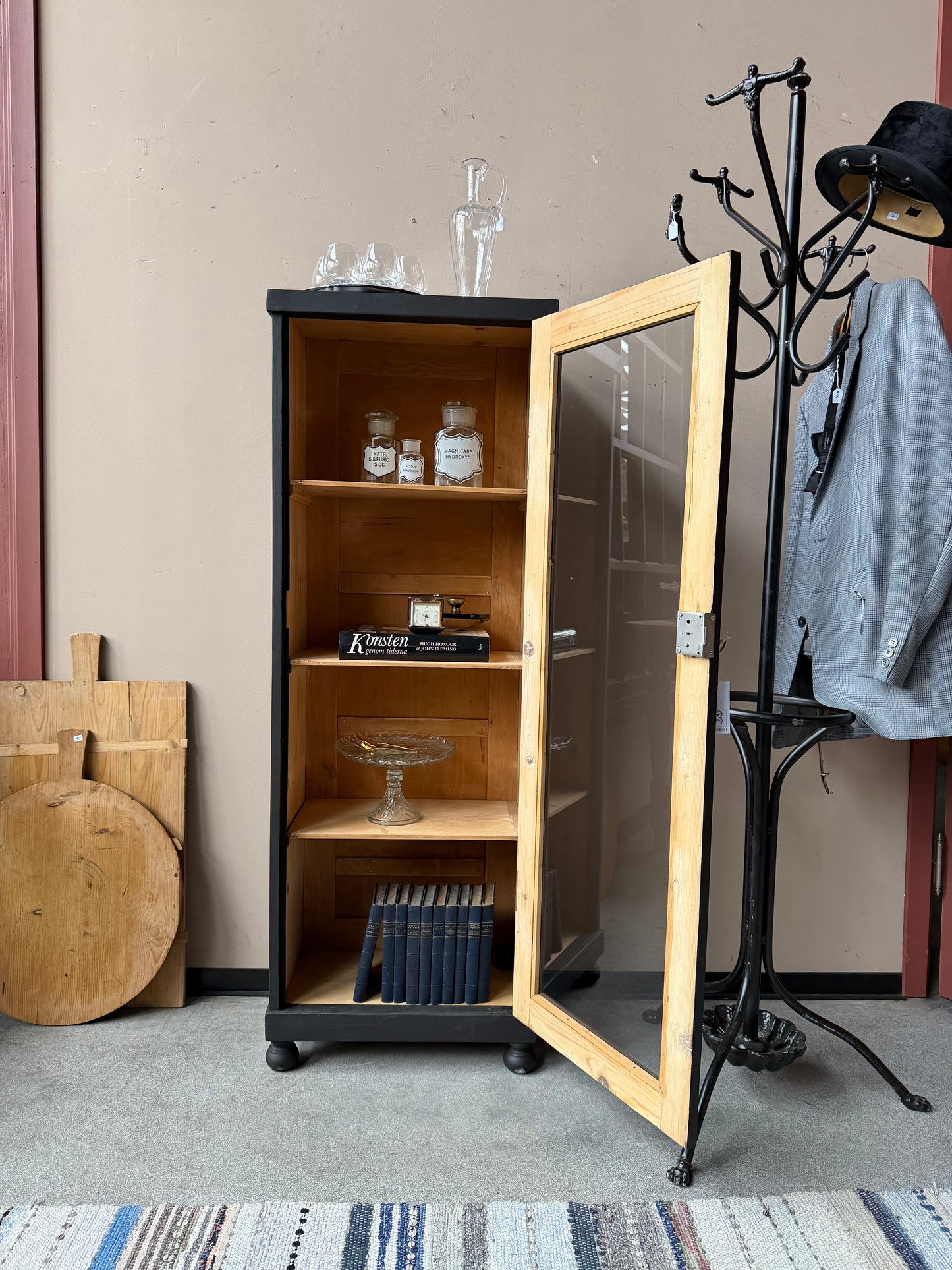 Ett gammalt vackert svart 1-dörrars vitrinskåp med glas i dörren. Skåpet har ett klassiskt uttryck.