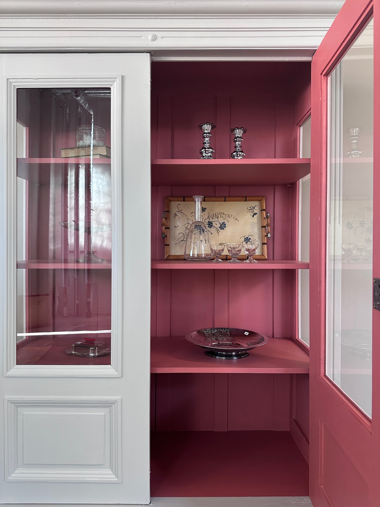 Bild visar ljust vitrinskåp med två dörrar, varav den ena är öppen. Insidan på skåpet är rosa