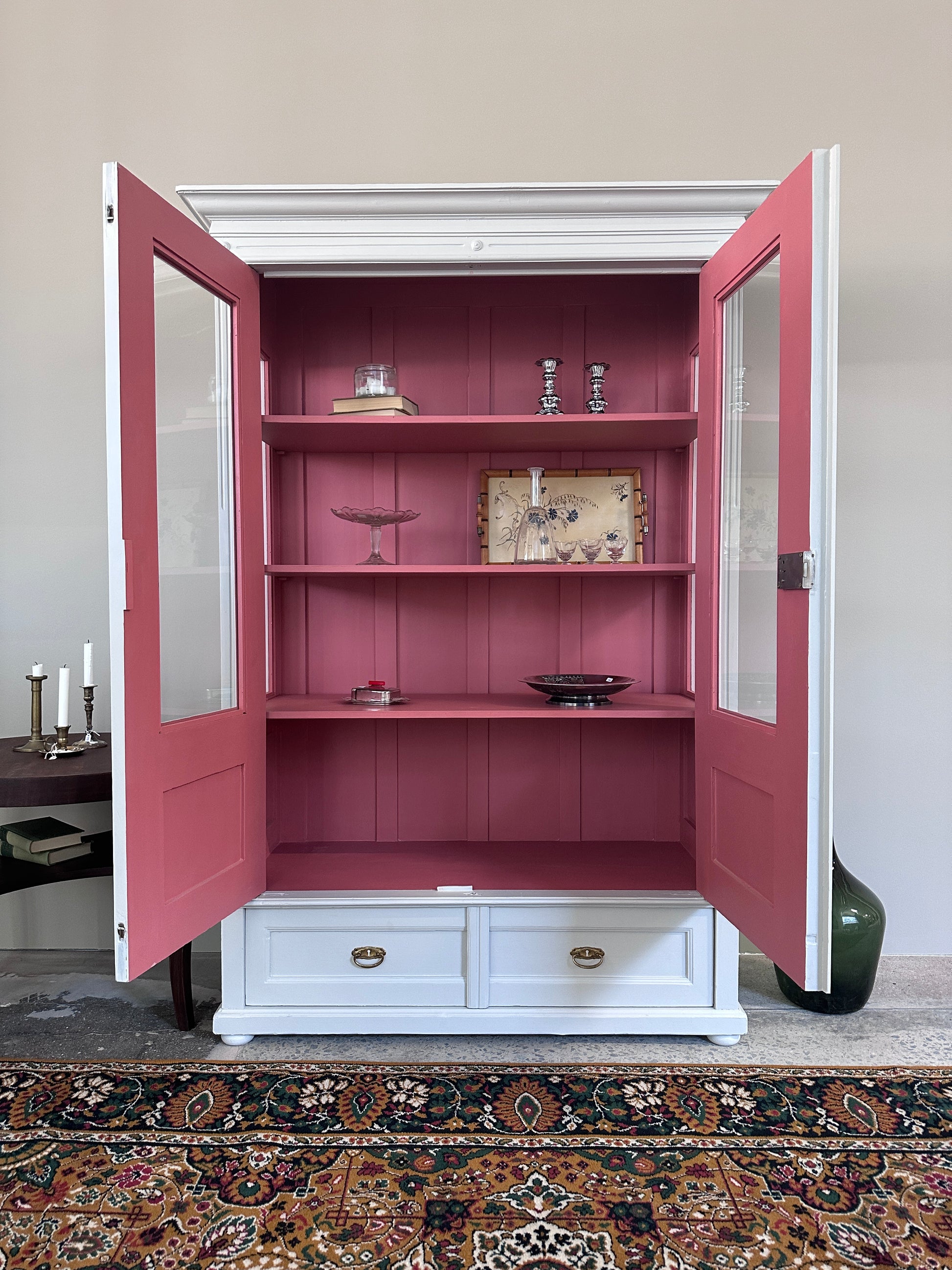 Bild visar ljust vitrinskåp med två dörrar, båda dörrarna är öppna. Insidan på skåpet är rosa