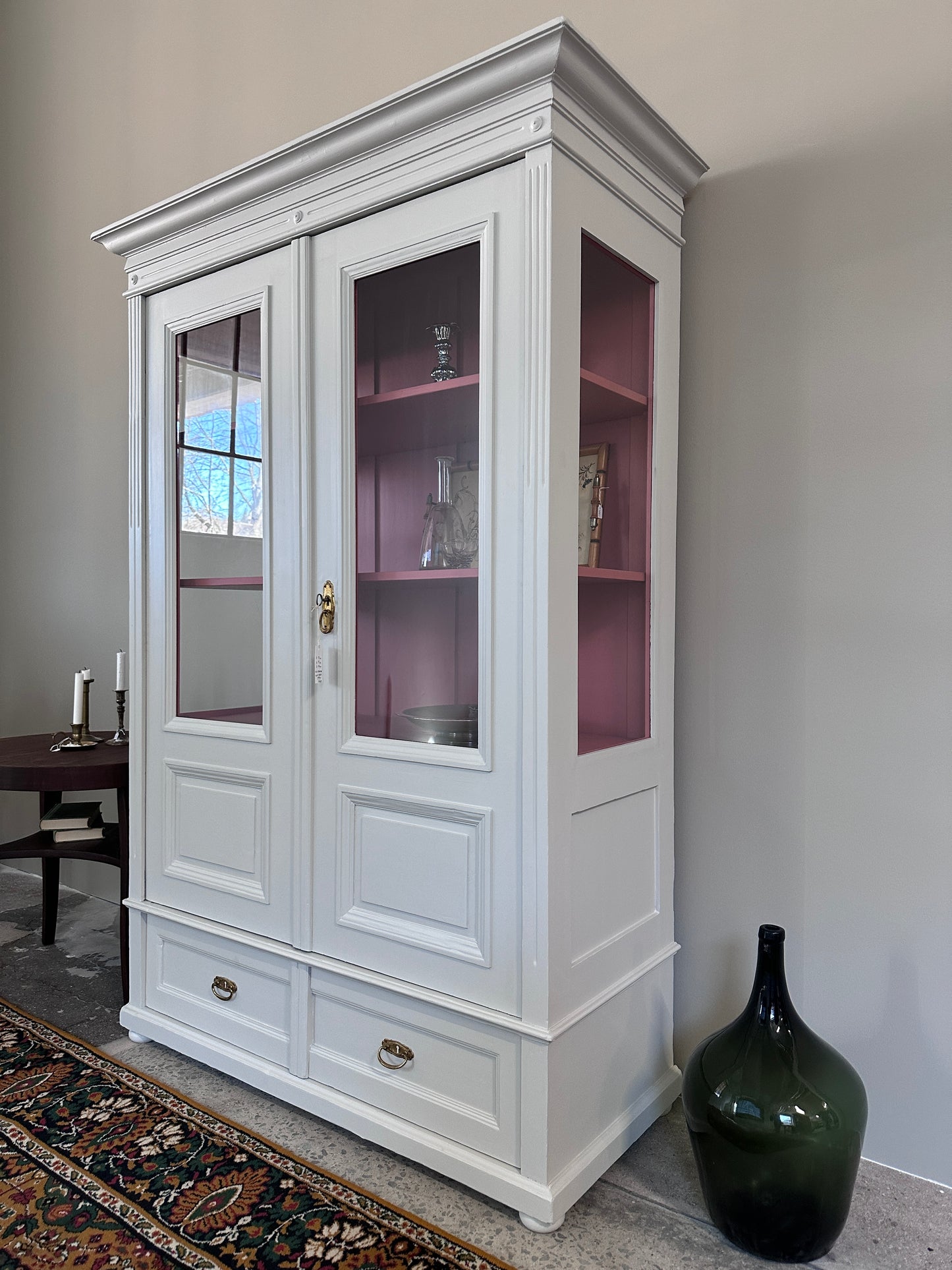 Bild visar ljust vitrinskåp med två dörrar.  Bild tagen från sidan. Insidan på skåpet är rosa