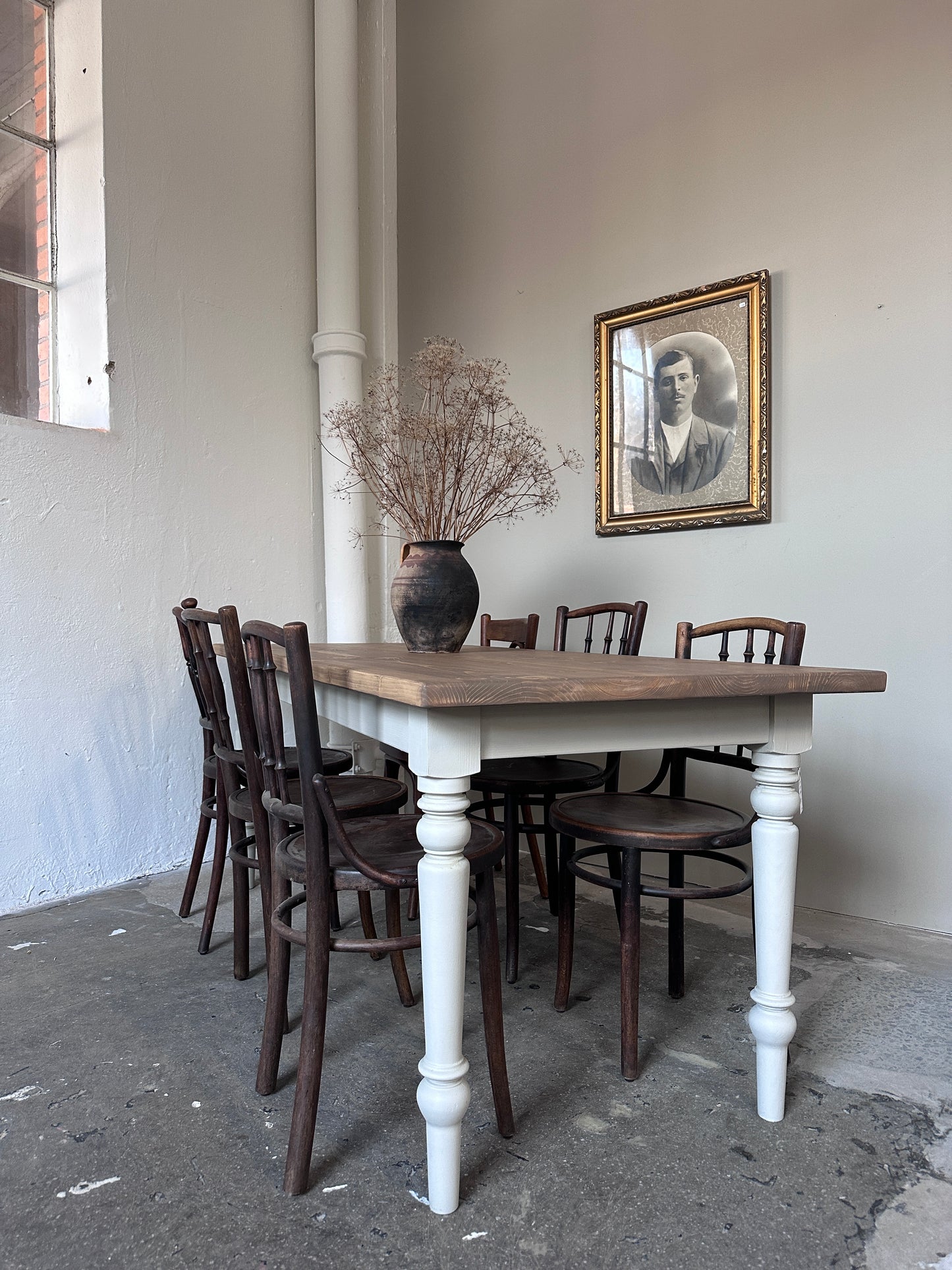 Bord med tre stolar på respektive långsida. På bordet står en urna med torkade kvistar och på väggen hänger en gammal tavla.