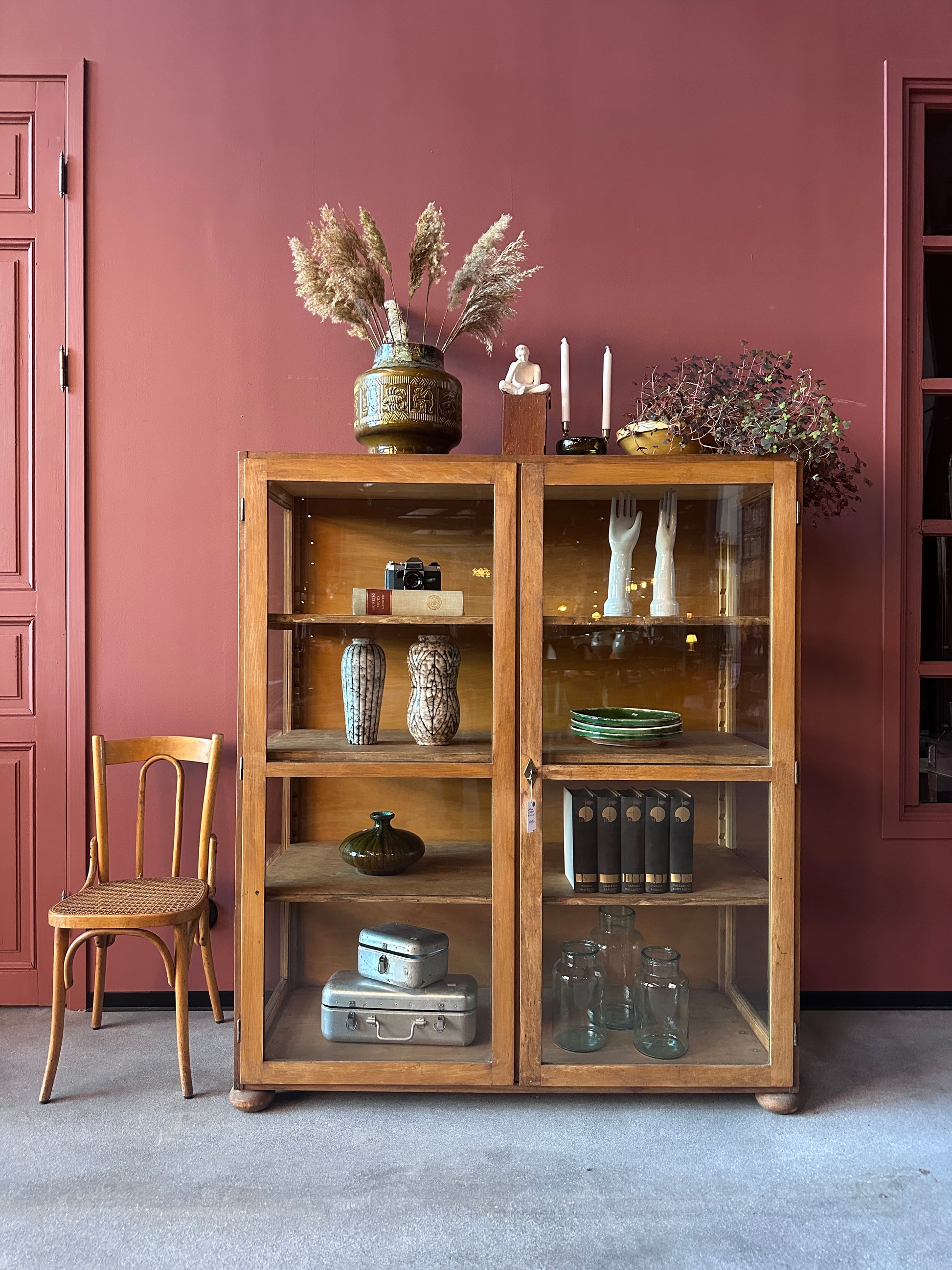Ett vitrinskåp mot en röd vägg men inredningsdetaljer.