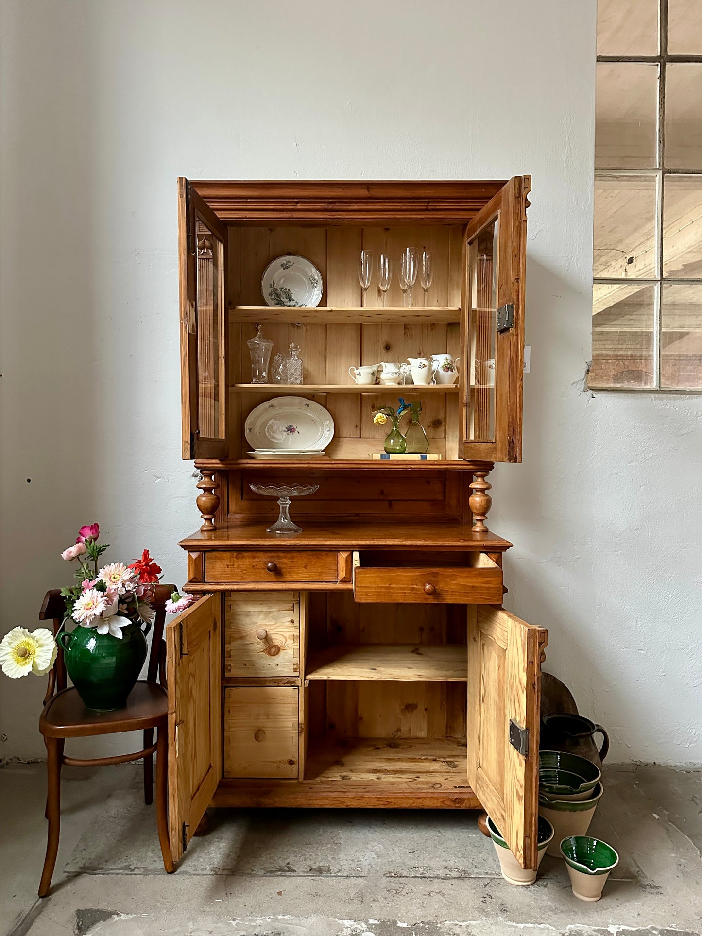 Ett gammalt, vackert köksskåp med symmetrisk utformning och mängder av förvaringsmöjligheter. På bilden är skåpsdörrar öppna.