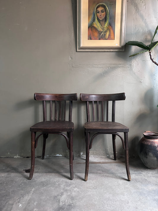 2 styck stolar i mörkt trä. Bilden är tagen rakt framifrån. På golvet står en urna och på väggen hänger en tavla. 