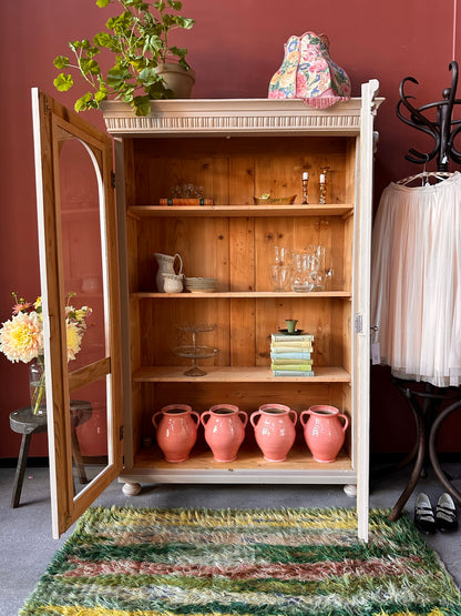 Ett vackert gammalt vitrinskåp med utsmyckade detaljer och rundade vitringlas utmed halva dörrarna.