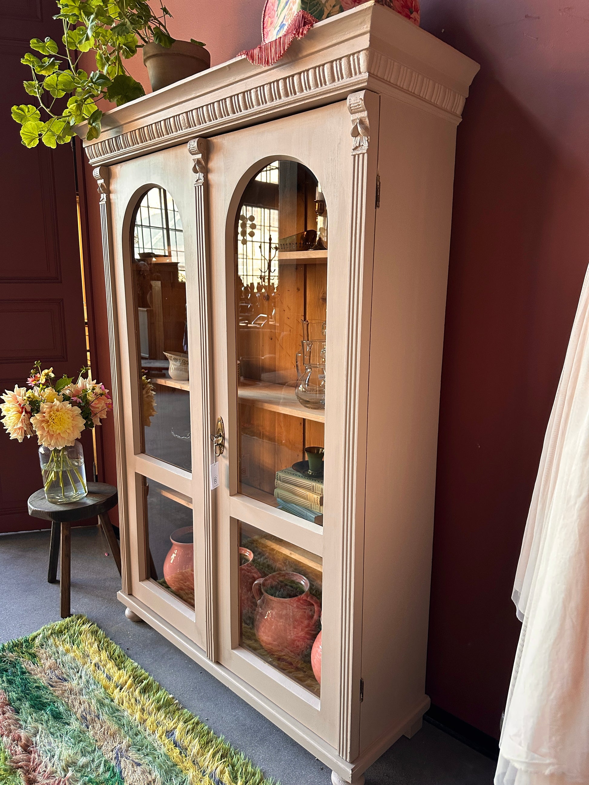 Ett vackert gammalt vitrinskåp med utsmyckade detaljer och rundade vitringlas utmed halva dörrarna.