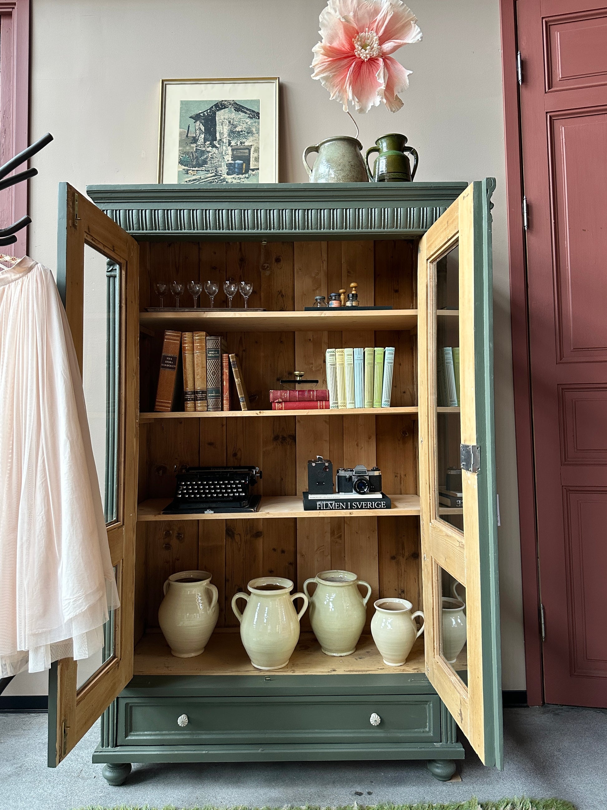 Ett gammalt vackert vitrinskåp med vackra detaljer. Skåpet har en bred praktiskt låda nertill med nya porslinsknoppar i äldre stil.