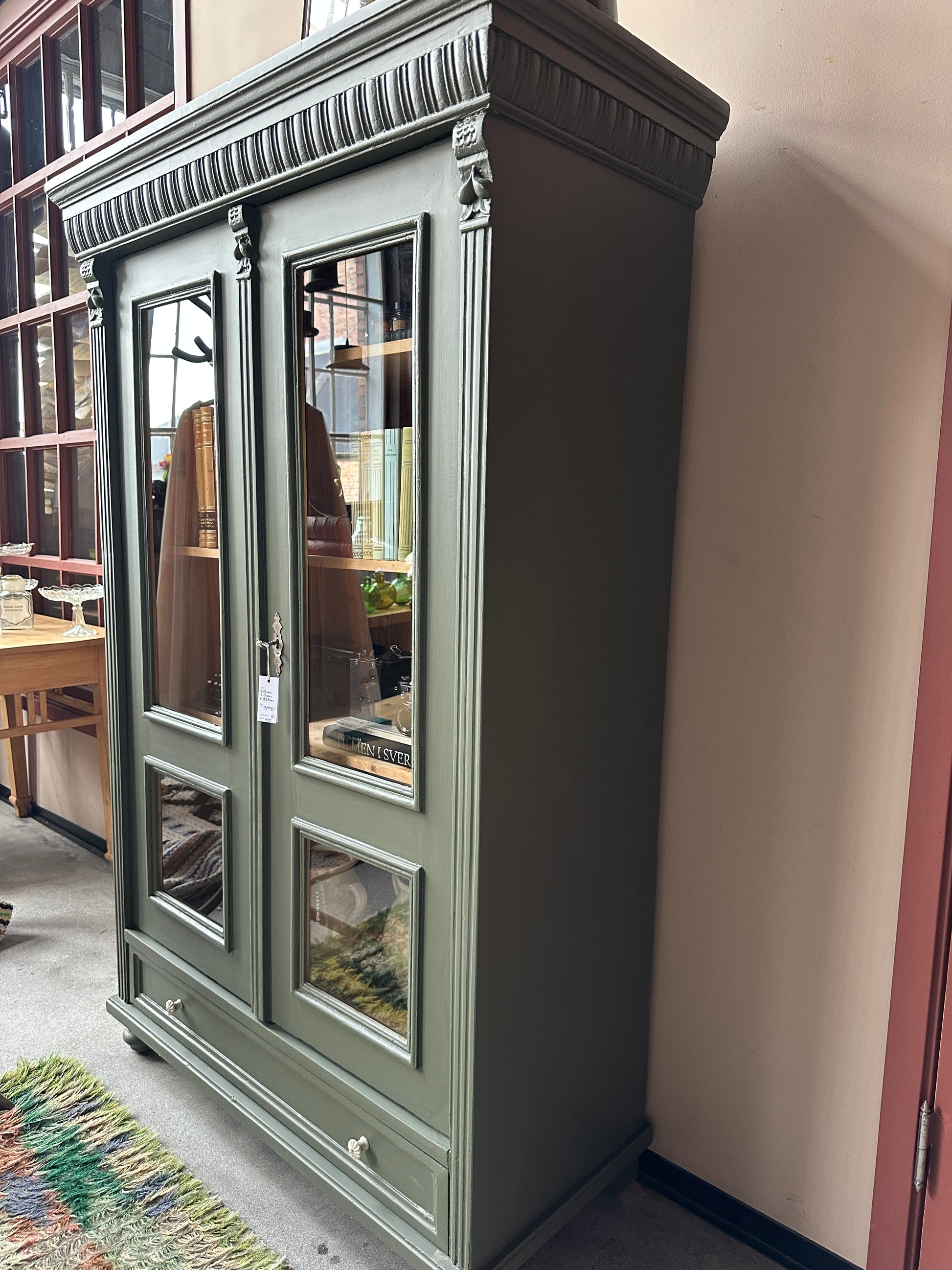 Ett gammalt vackert vitrinskåp med vackra detaljer. Skåpet har en bred praktiskt låda nertill med nya porslinsknoppar i äldre stil.