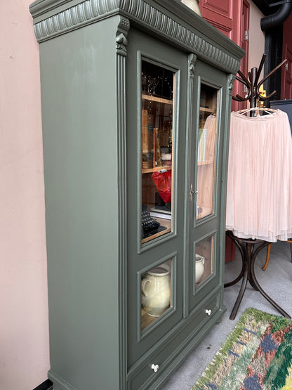 Ett gammalt vackert vitrinskåp med vackra detaljer. Skåpet har en bred praktiskt låda nertill med nya porslinsknoppar i äldre stil.