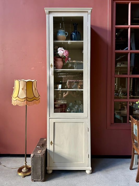 Ett högt vitrinskåp i greige kulör