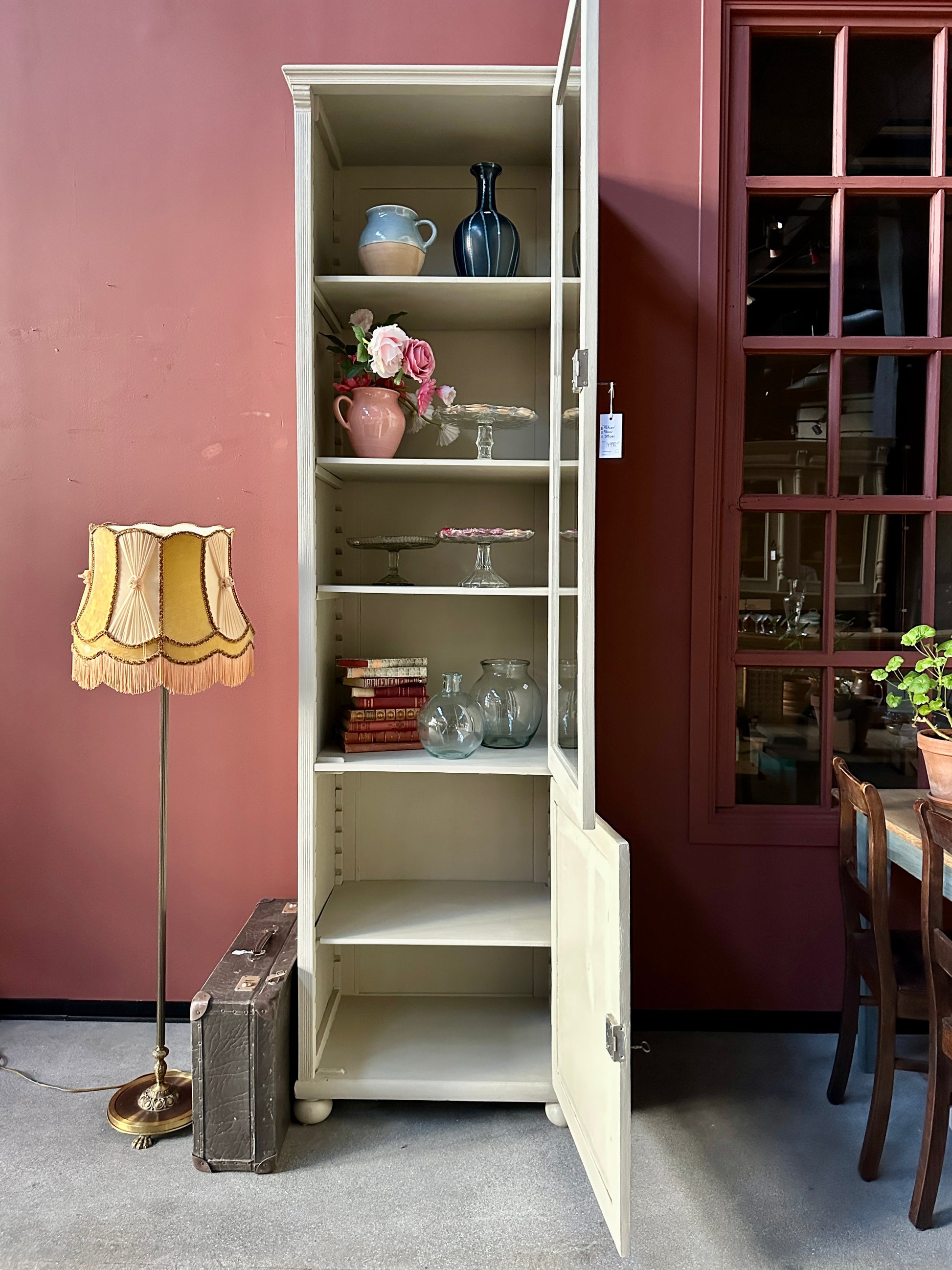 Ett högt vitrinskåp i greige kulör. öppna dörrar