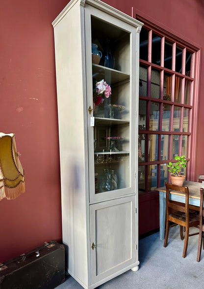 Ett högt vitrinskåp i greige kulör