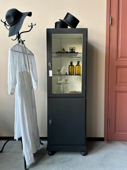 Ett gammalt klassiskt läkarskåp med två hyllor i glas.&nbsp;
Skåpet har både dörr med glas samt täckt dörr nertill.