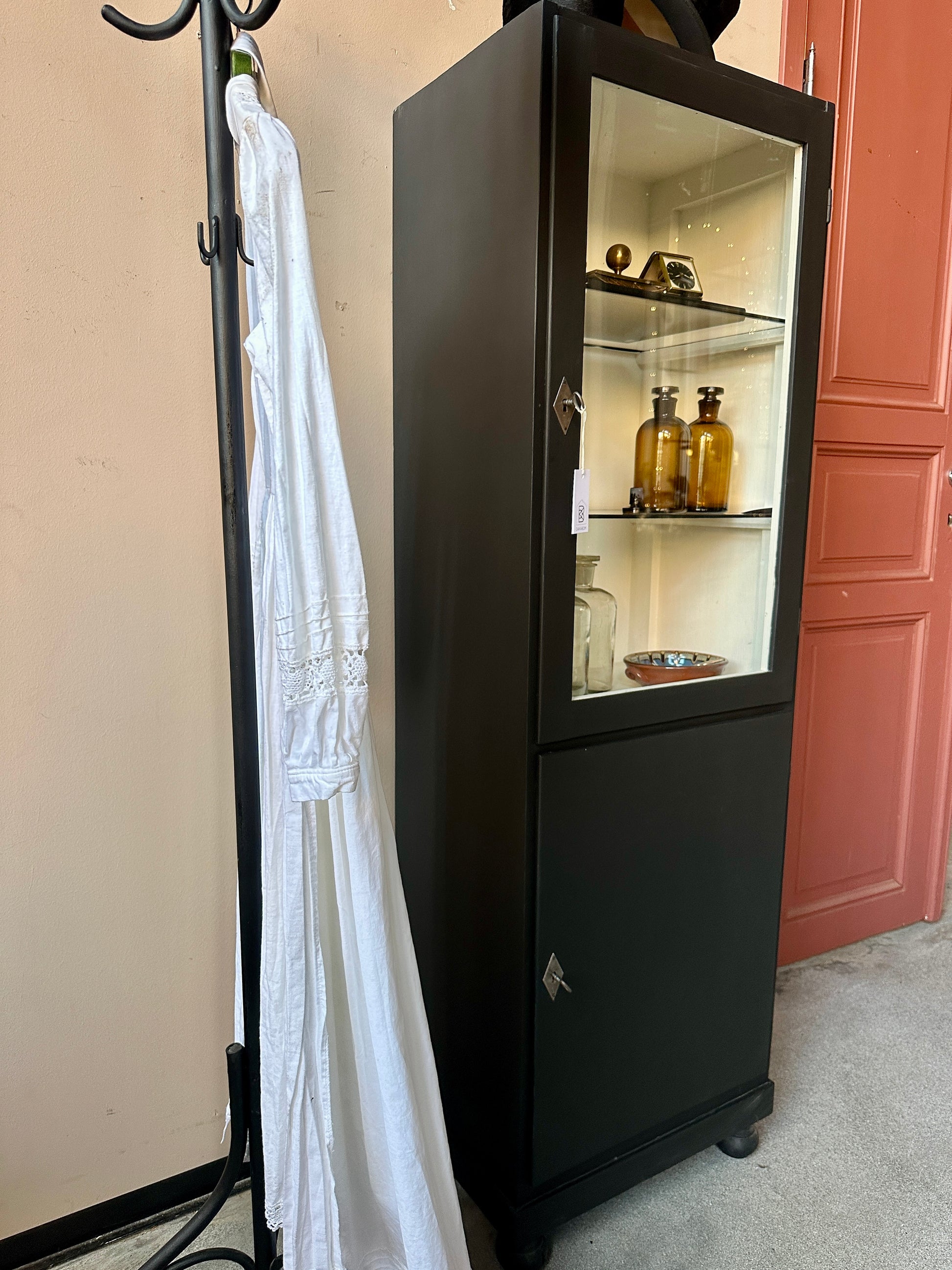 Ett gammalt klassiskt läkarskåp med två hyllor i glas.&nbsp;
Skåpet har både dörr med glas samt täckt dörr nertill.