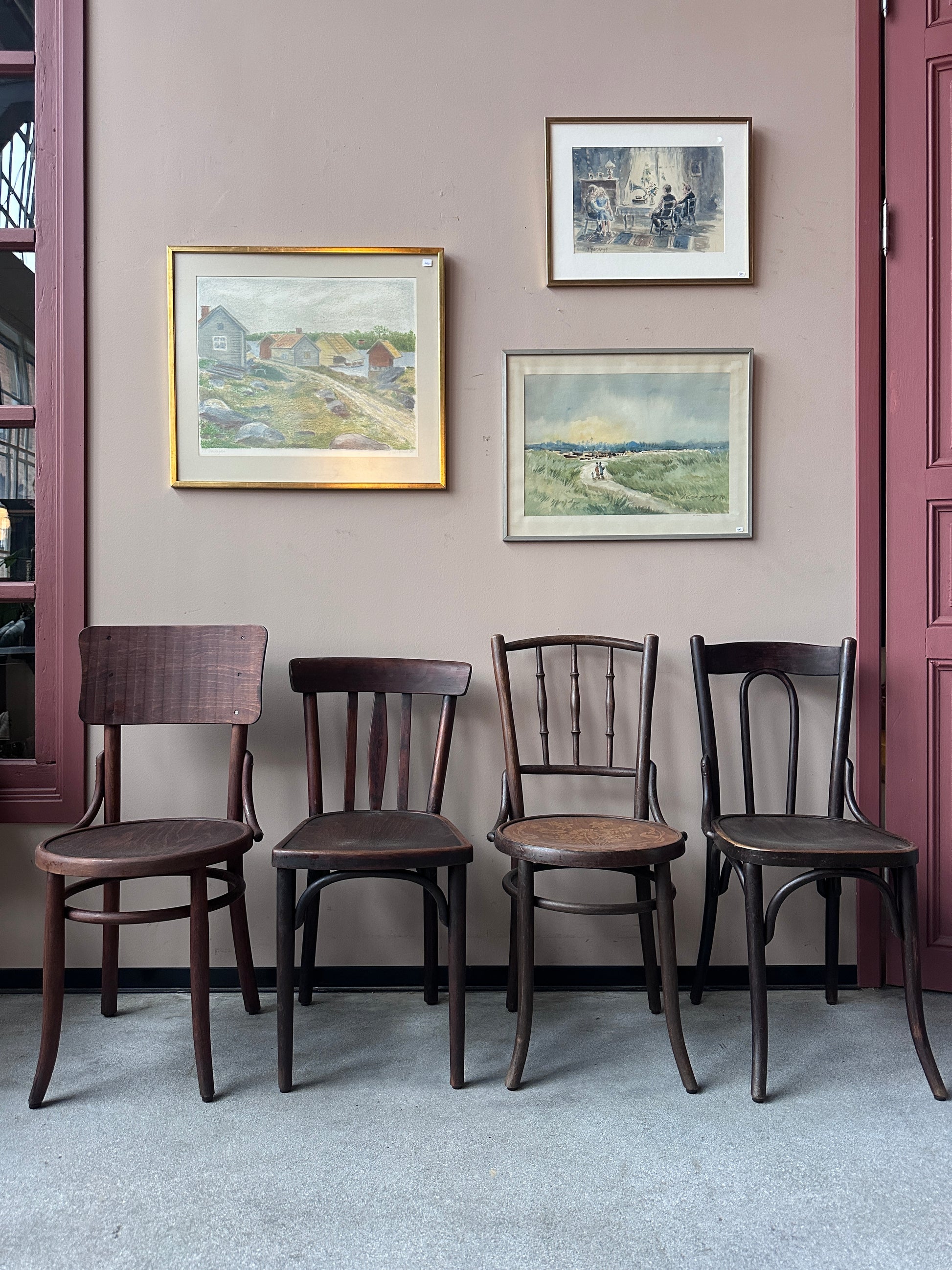 4 st bruna stolar i olika modeller. Stolarna står mot en vägg med 3 st tavlor. 
