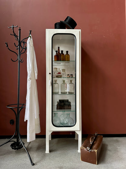 Ett gammalt läckert läkarskåp med fyra hyllor i glas och även glas i sidan.&nbsp;
Skåpet är i stål och lackat vitt