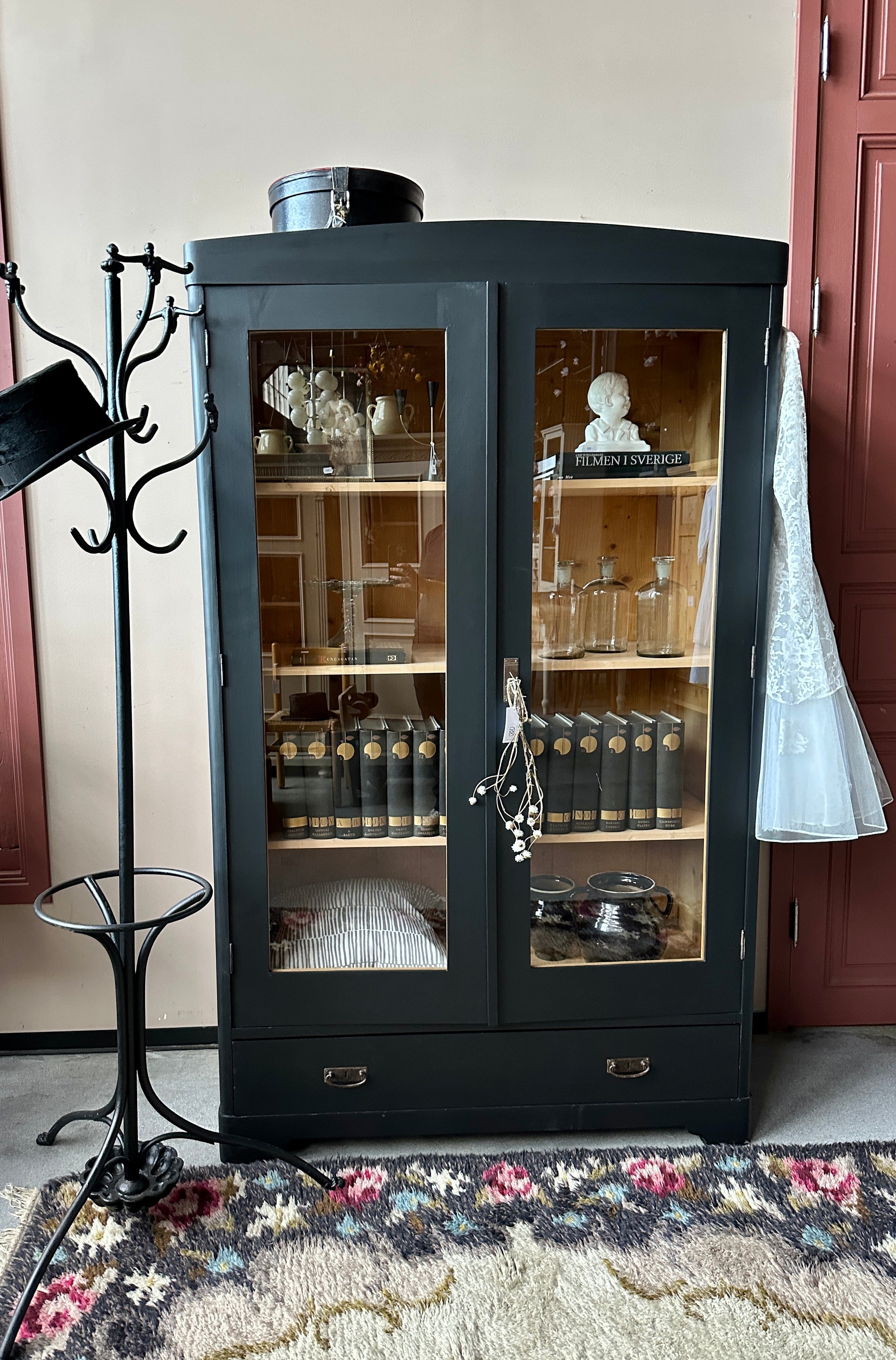 Ett gammalt, vackert vitrinskåp med rundad överkant.Skåpet har två glasdörrar.