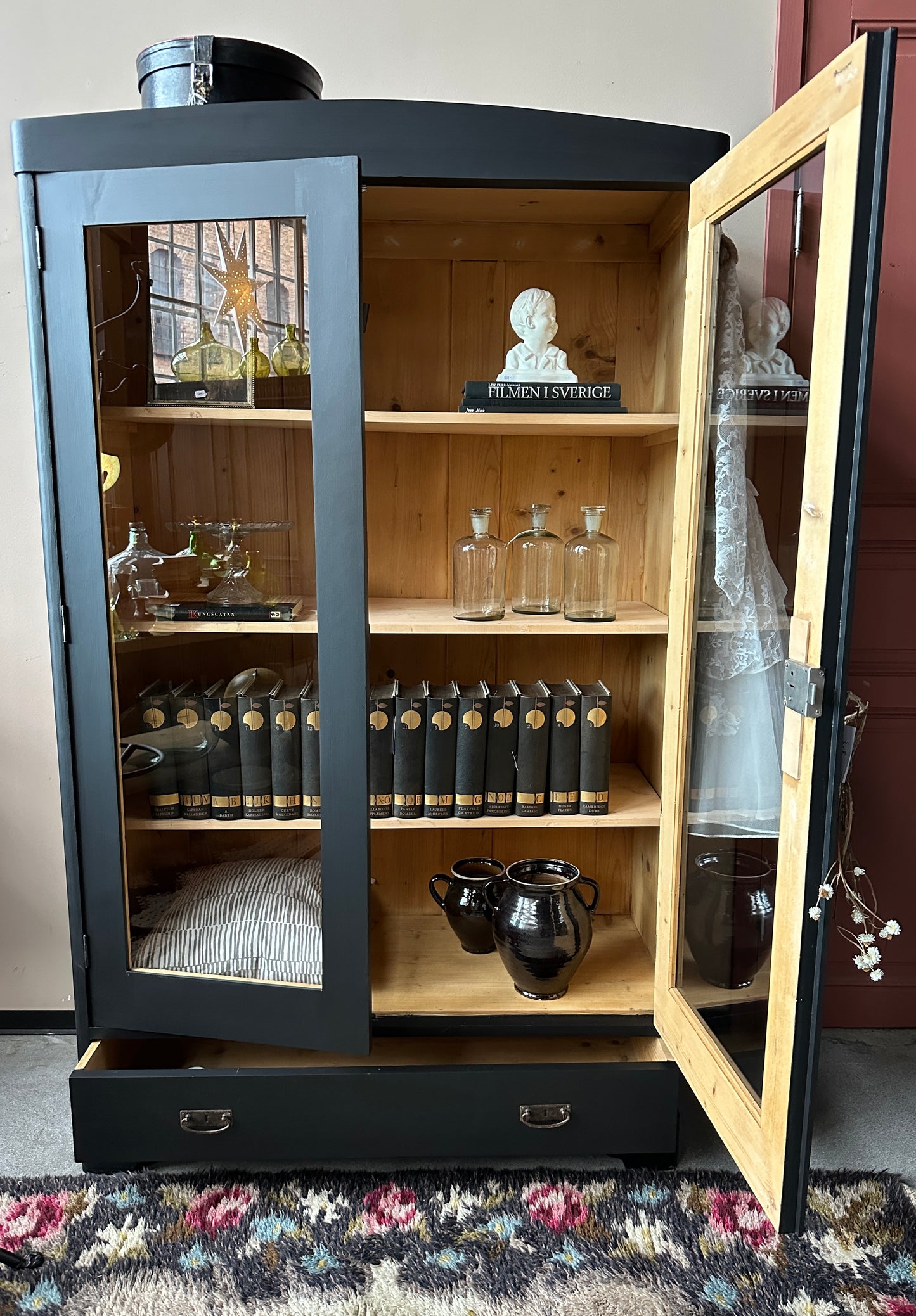 Ett gammalt, vackert vitrinskåp med rundad överkant.Skåpet har två glasdörrar.