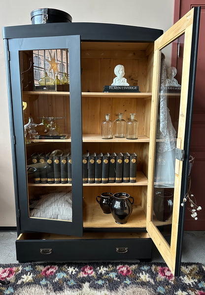 Ett gammalt, vackert vitrinskåp med rundad överkant.Skåpet har två glasdörrar.