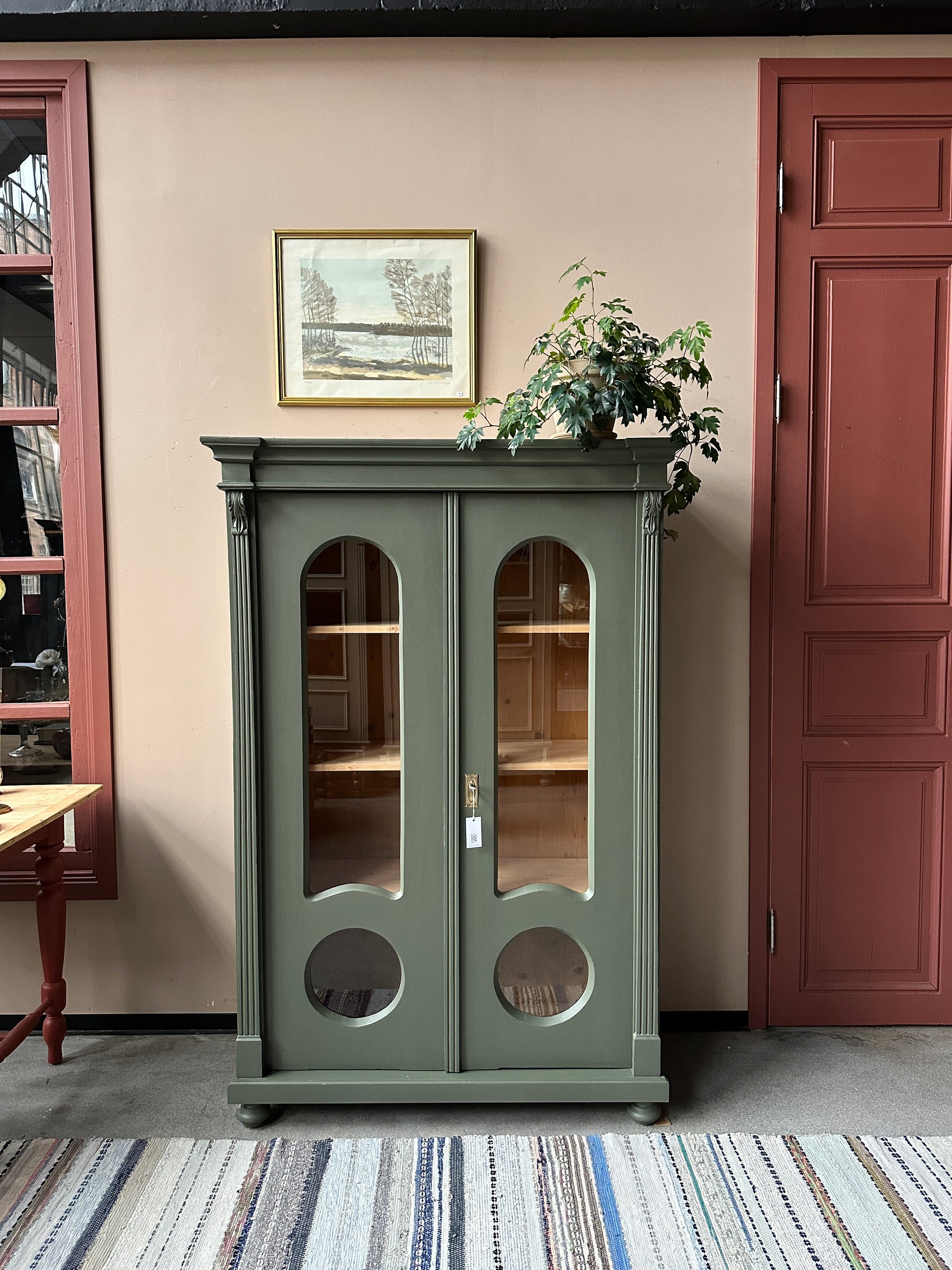 Ett gammalt, vackert vitrinskåp med fina detaljer i de rundade formerna och det arbetade krönet.