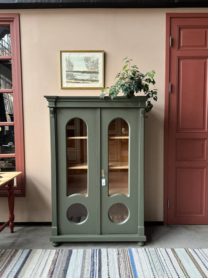 Ett gammalt, vackert vitrinskåp med fina detaljer i de rundade formerna och det arbetade krönet.