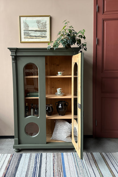 Ett gammalt, vackert vitrinskåp med fina detaljer i de rundade formerna och det arbetade krönet.