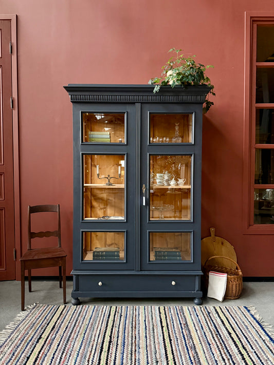 Ett gammalt, otroligt vackert vitrinskåp med fina detaljer i de raka formerna.Skåpet har i dagsläget 3 st nya och fräscha hyllplan, vi kan sätta in fler om det önskas. Det har dessutom en bred praktisk låda längst ner med vackra porslinsknoppar.Skåpet är varsamt renoverat och slutligen penselmålat med en matt, vattenbaserad snickerifärg i Dakaboms åskblåa kulör.