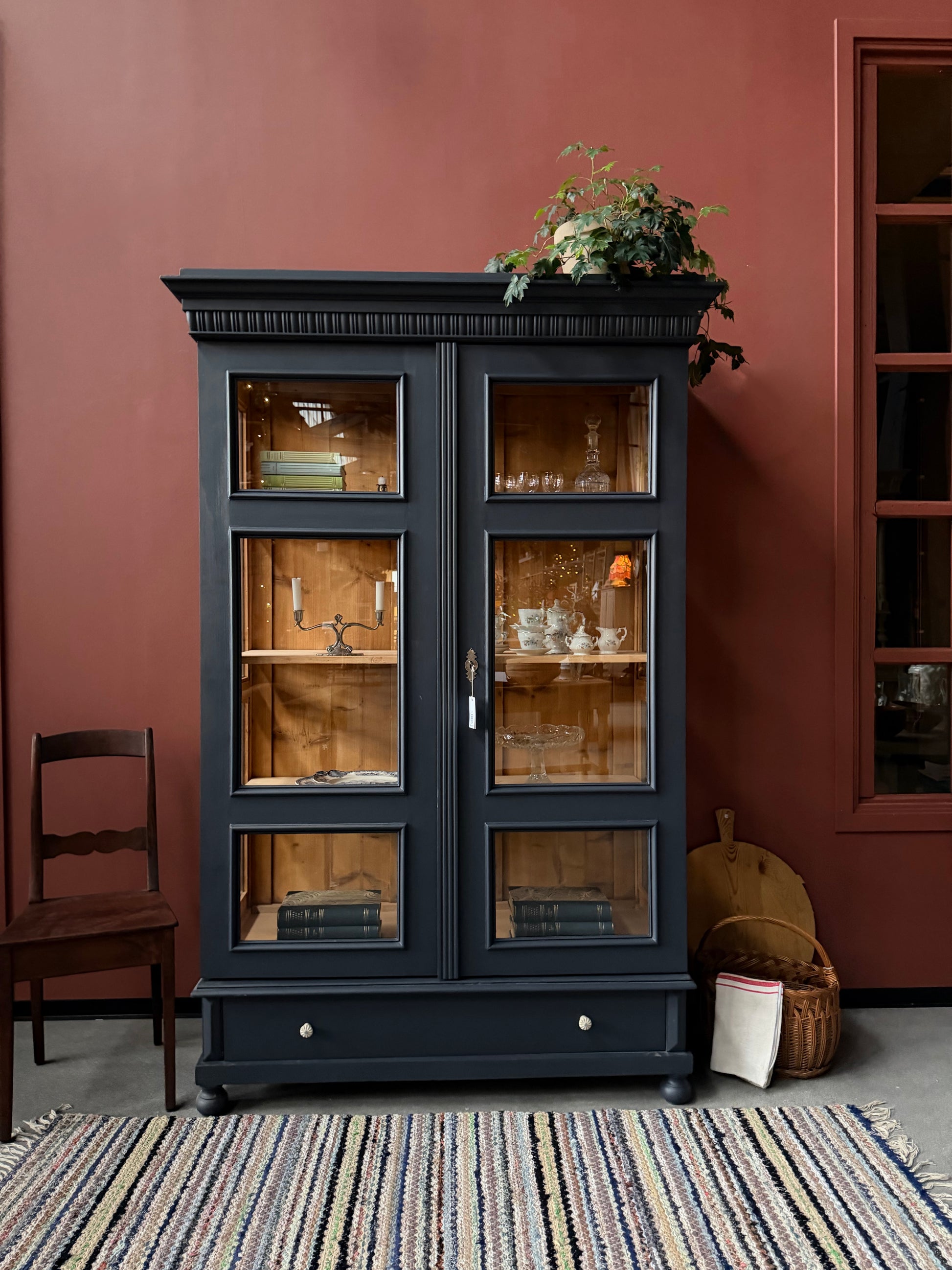 Ett gammalt, otroligt vackert vitrinskåp med fina detaljer i de raka formerna.Skåpet har i dagsläget 3 st nya och fräscha hyllplan, vi kan sätta in fler om det önskas. Det har dessutom en bred praktisk låda längst ner med vackra porslinsknoppar.Skåpet är varsamt renoverat och slutligen penselmålat med en matt, vattenbaserad snickerifärg i Dakaboms åskblåa kulör.