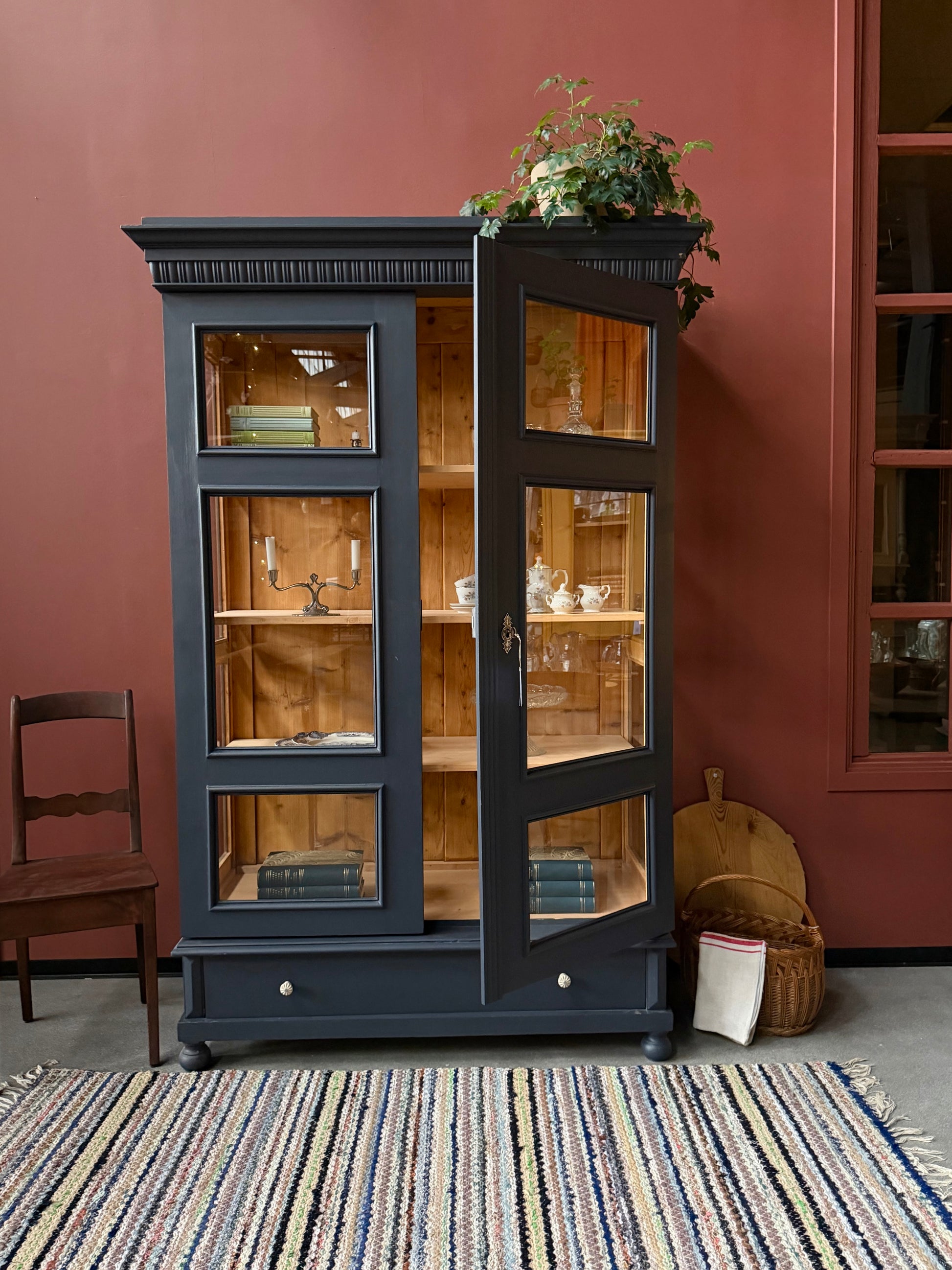 Ett gammalt, otroligt vackert vitrinskåp med fina detaljer i de raka formerna.Skåpet har i dagsläget 3 st nya och fräscha hyllplan, vi kan sätta in fler om det önskas. Det har dessutom en bred praktisk låda längst ner med vackra porslinsknoppar.Skåpet är varsamt renoverat och slutligen penselmålat med en matt, vattenbaserad snickerifärg i Dakaboms åskblåa kulör.