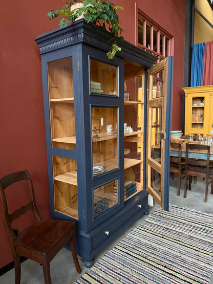 Ett gammalt, otroligt vackert vitrinskåp med fina detaljer i de raka formerna.Skåpet har i dagsläget 3 st nya och fräscha hyllplan, vi kan sätta in fler om det önskas. Det har dessutom en bred praktisk låda längst ner med vackra porslinsknoppar.Skåpet är varsamt renoverat och slutligen penselmålat med en matt, vattenbaserad snickerifärg i Dakaboms åskblåa kulör.