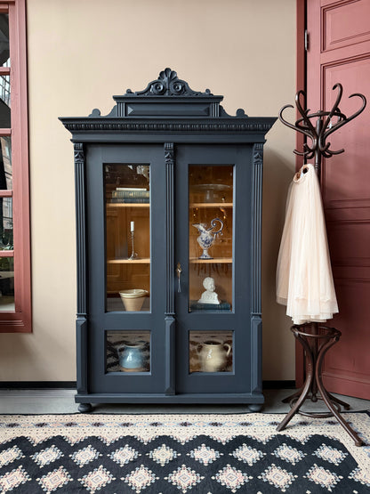 Ett gammalt vackert vitrinskåp med många vackra detaljer. Skåpet har glas hela vägen ner i dörrarna, spår i sidorna, dekorationer i hörnen samt ett vackert utsmyckat ornament uppe på krönet som går att ta bort om man föredrar det.