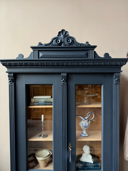 Ett gammalt vackert vitrinskåp med många vackra detaljer. Skåpet har glas hela vägen ner i dörrarna, spår i sidorna, dekorationer i hörnen samt ett vackert utsmyckat ornament uppe på krönet som går att ta bort om man föredrar det.