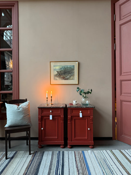 Ett par gamla, vackra sängbord med fin utsmyckning och klassisk form med både låda och skåp. Sängborden har en fantastiskt vacker svart/vit marmorerad toppskiva i sten som är avtagbar. Sängborden är varsamt renoverade och slutligen penselmålade med en matt snickerifärg i Dakaboms varmröda kulör.