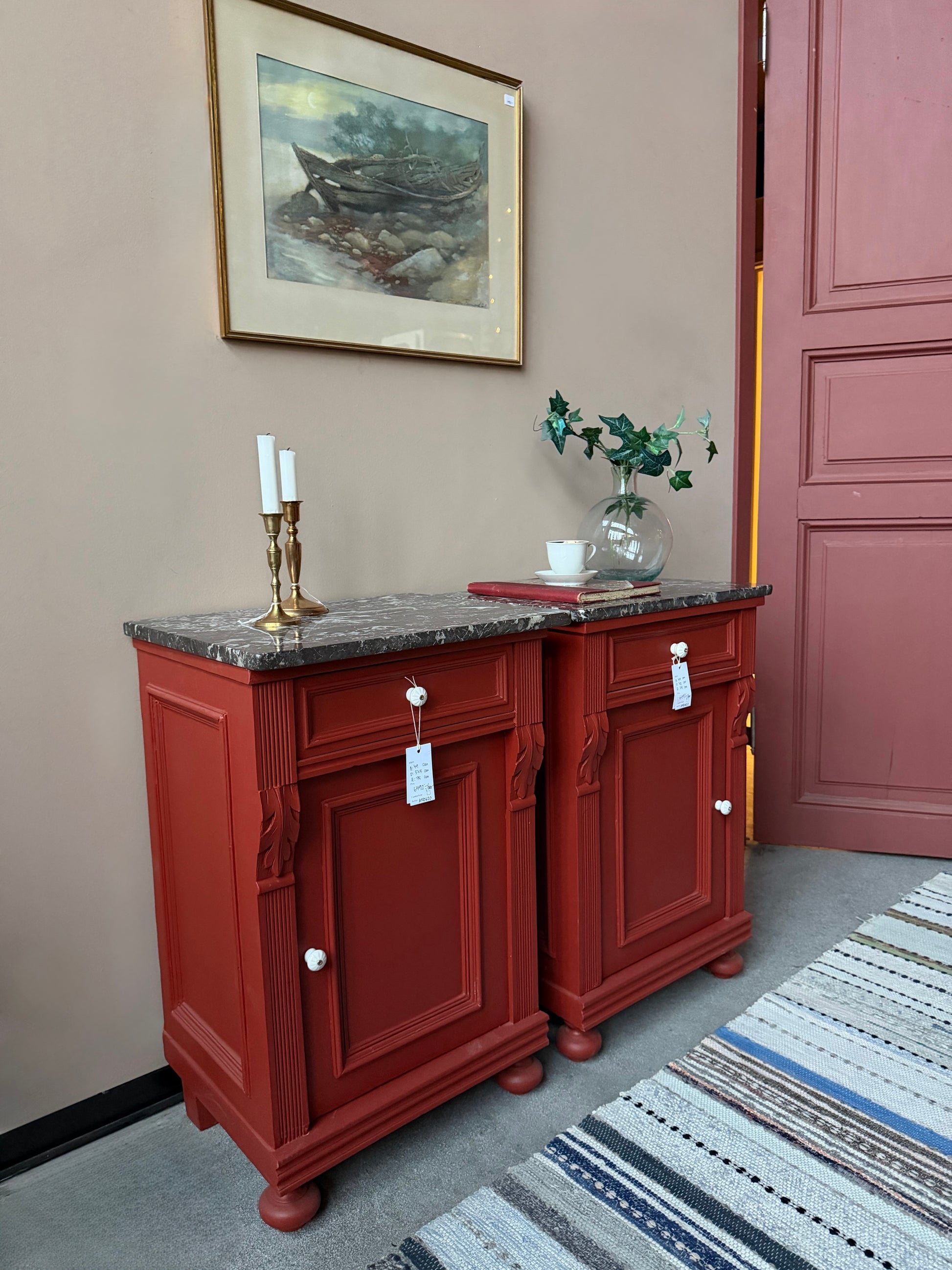 Ett par gamla, vackra sängbord med fin utsmyckning och klassisk form med både låda och skåp. Sängborden har en fantastiskt vacker svart/vit marmorerad toppskiva i sten som är avtagbar. Sängborden är varsamt renoverade och slutligen penselmålade med en matt snickerifärg i Dakaboms varmröda kulör.