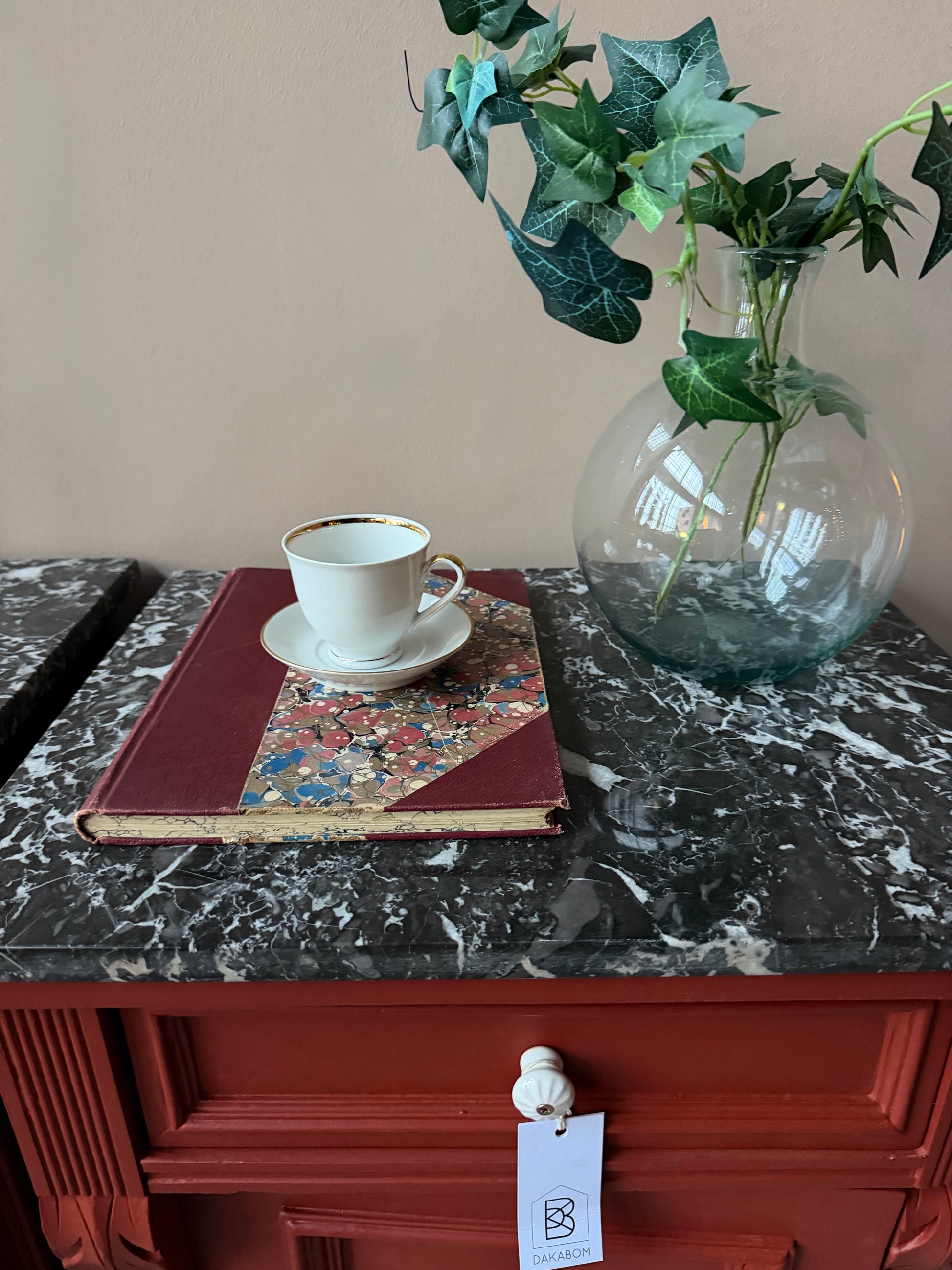 Ett par gamla, vackra sängbord med fin utsmyckning och klassisk form med både låda och skåp. Sängborden har en fantastiskt vacker svart/vit marmorerad toppskiva i sten som är avtagbar. Sängborden är varsamt renoverade och slutligen penselmålade med en matt snickerifärg i Dakaboms varmröda kulör.