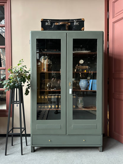 Ett gammalt vackert vitrinskåp men raka och mjuka former och enkla detaljer. Skåpet har en bred praktiskt låda nertill med nya knoppar i äldre stil.