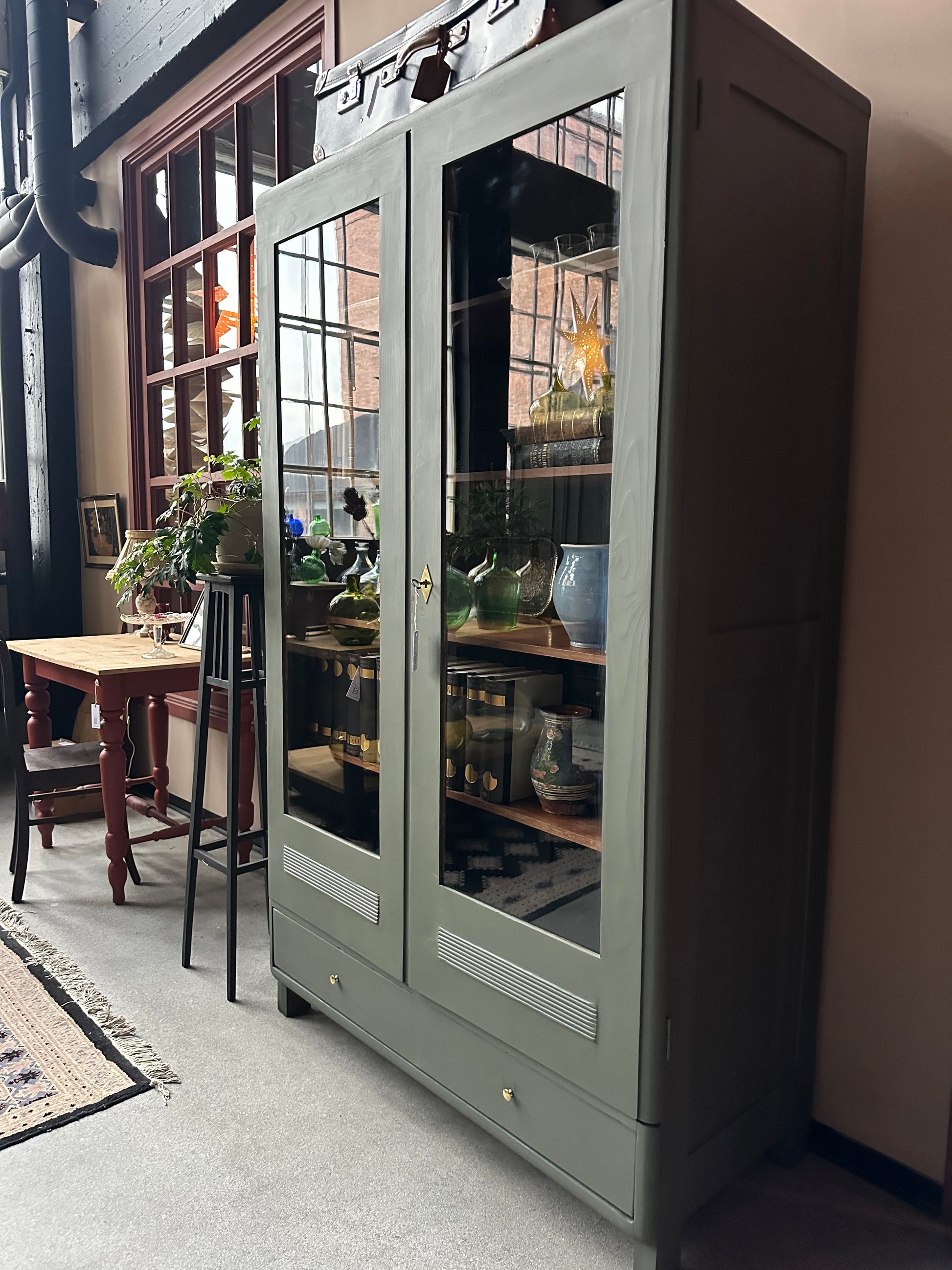 Ett gammalt vackert vitrinskåp men raka och mjuka former och enkla detaljer. Skåpet har en bred praktiskt låda nertill med nya knoppar i äldre stil.