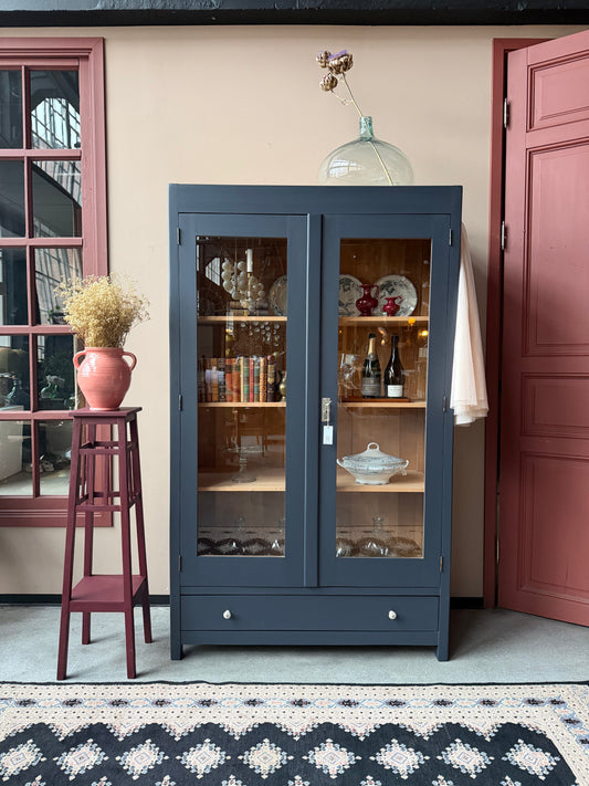 Ett gammalt vackert vitrinskåp med raka former och vitrin. Skåpet har glas hela vägen ner i dörrarna.  Längst ner finns en praktisk låda med fina porslinsknoppar. Skåpet är varsamt renoverat och sedan penselmålat med en matt snickerifärg i Dakaboms åskblåa kulör.