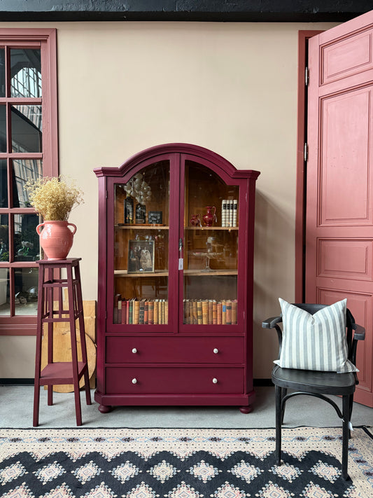 Ett gammalt, elegant vitrinskåp med runda former. Skåpet är nätt och unikt, målat i den ljuvliga kulören Burgundy.