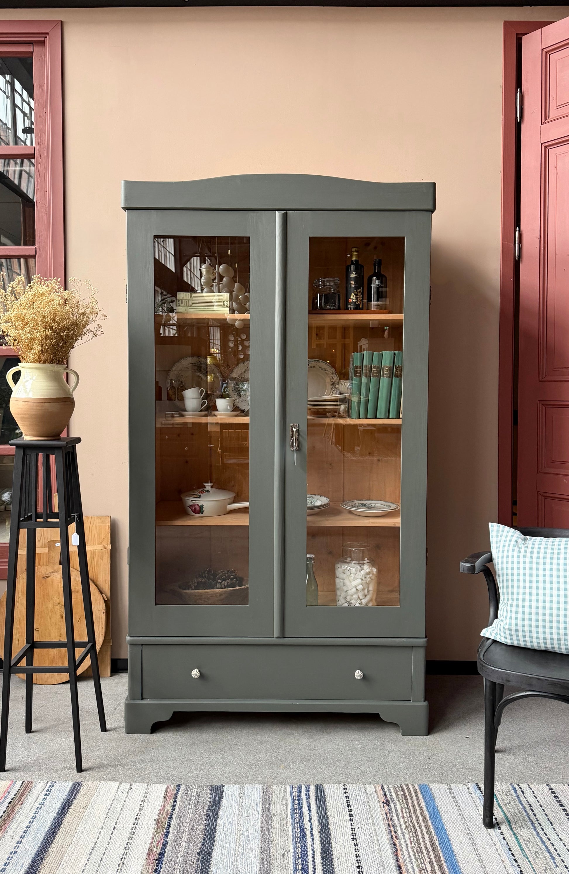 Ett gammalt vackert vitrinskåp med både runda och raka former i Dakaboms mörka grågröna färg. 