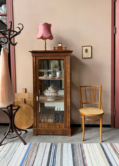 Ett gammalt, elegant vitrinskåp/displayskåp med ett stort glas samt glas i sidan för vackert ljusinsläpp. På skåpets insida sitter en spegel. 