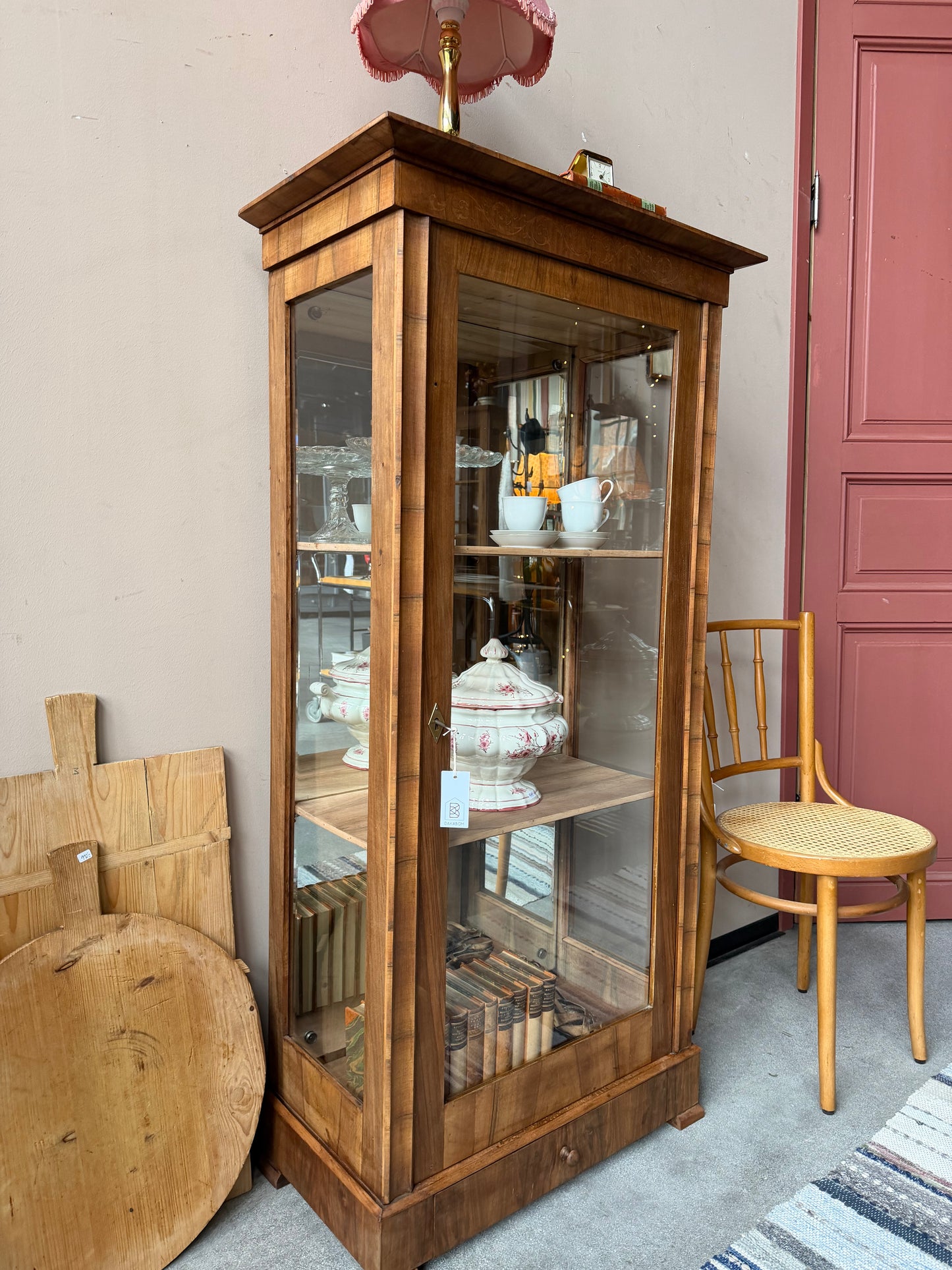 Ett gammalt, elegant vitrinskåp/displayskåp med ett stort glas samt glas i sidan för vackert ljusinsläpp. På skåpets insida sitter en spegel. 