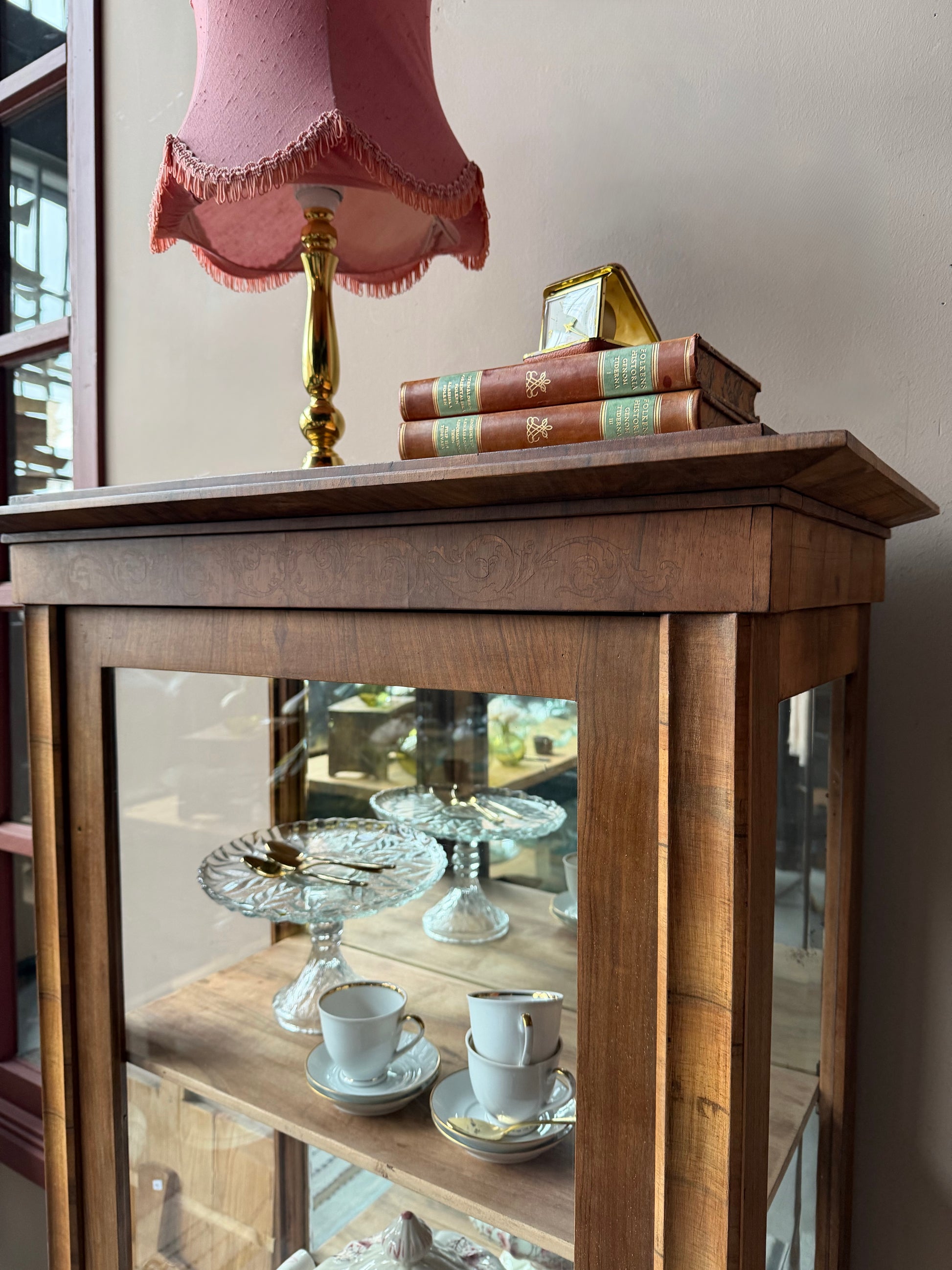 Ett gammalt, elegant vitrinskåp/displayskåp med ett stort glas samt glas i sidan för vackert ljusinsläpp. På skåpets insida sitter en spegel. 