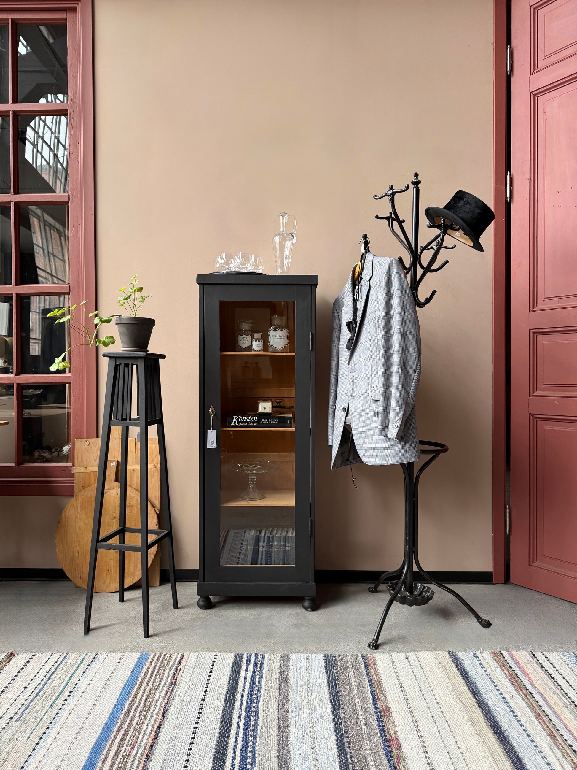 Ett gammalt vackert svart 1-dörrars vitrinskåp med glas i dörren. Skåpet har ett klassiskt uttryck.