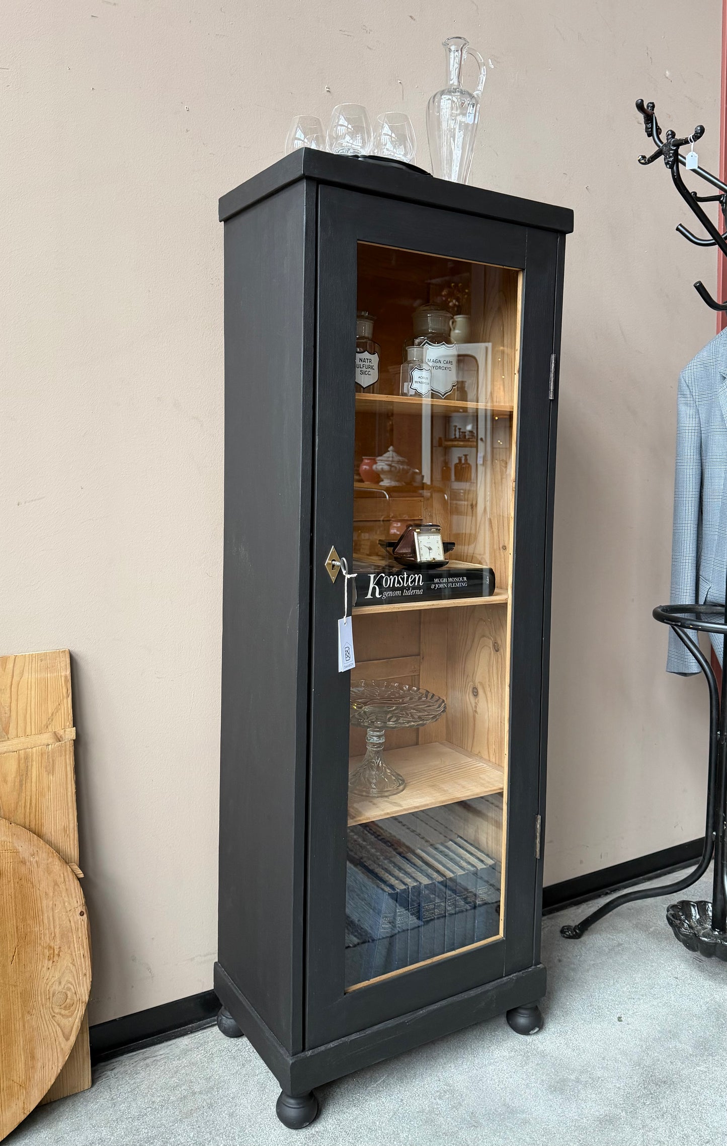 Ett gammalt vackert svart 1-dörrars vitrinskåp med glas i dörren. Skåpet har ett klassiskt uttryck.