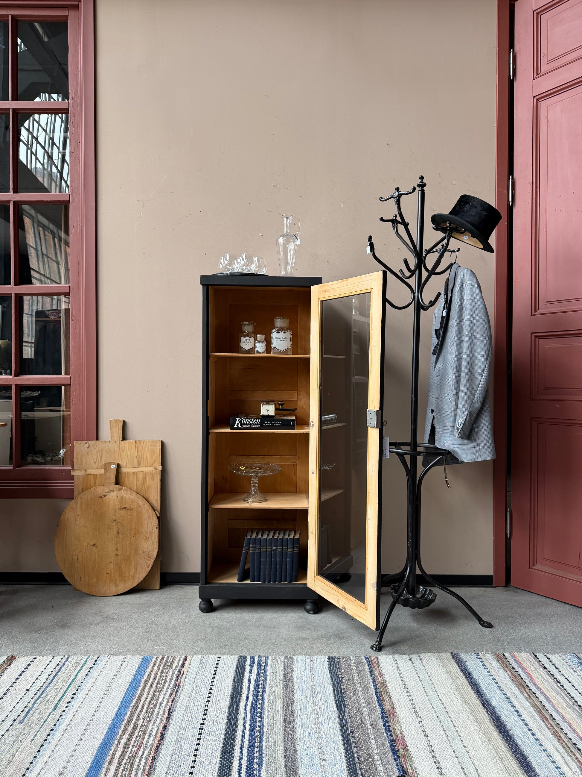 Ett gammalt vackert svart 1-dörrars vitrinskåp med glas i dörren. Skåpet har ett klassiskt uttryck.