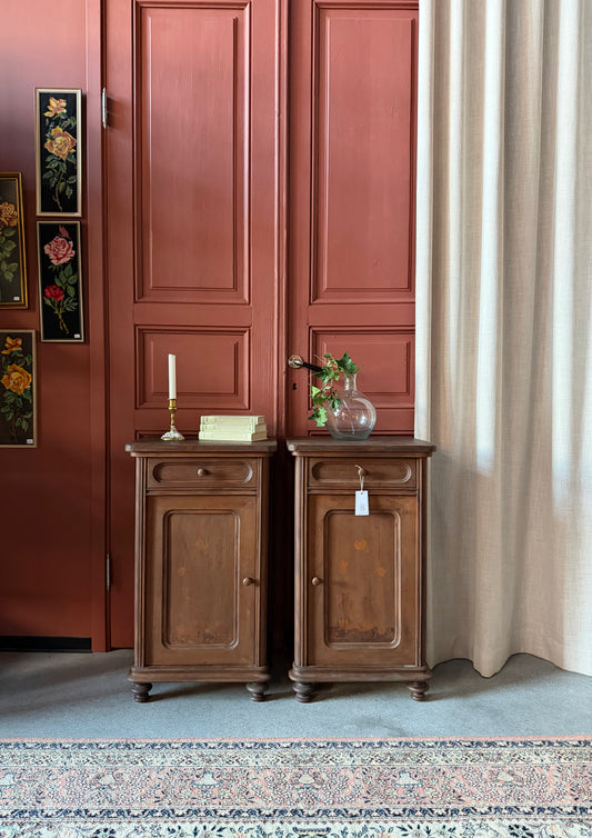 Ett par gamla, vackra sängbord i enkel och klassisk form med både låda och skåp. Sängborden har väldigt vacker utsmyckning med detaljer i form av blomsterrankor, näckrosor och svanar på dörrarna. 