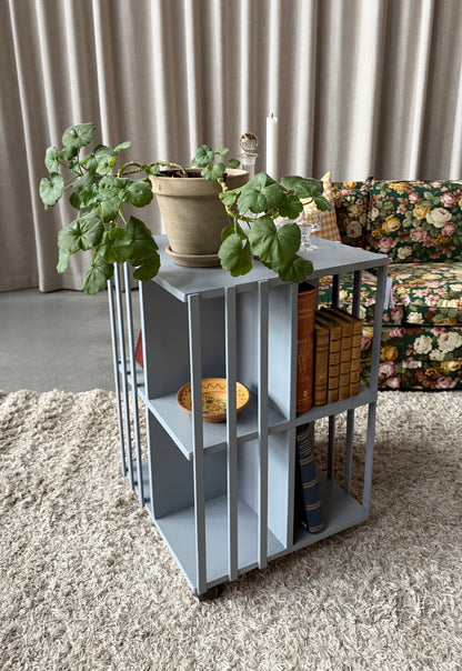 Ett vackert kvadratiskt sidebord/litet bord på hjul med ljuvliga små hyllor/fack på alla sidor vilket gör att det passar fint i rummet som sidebord att fylla med böcker och andra stilleben. Det är varsamt renoverat och målat i en ljust blå/grå kulör. 